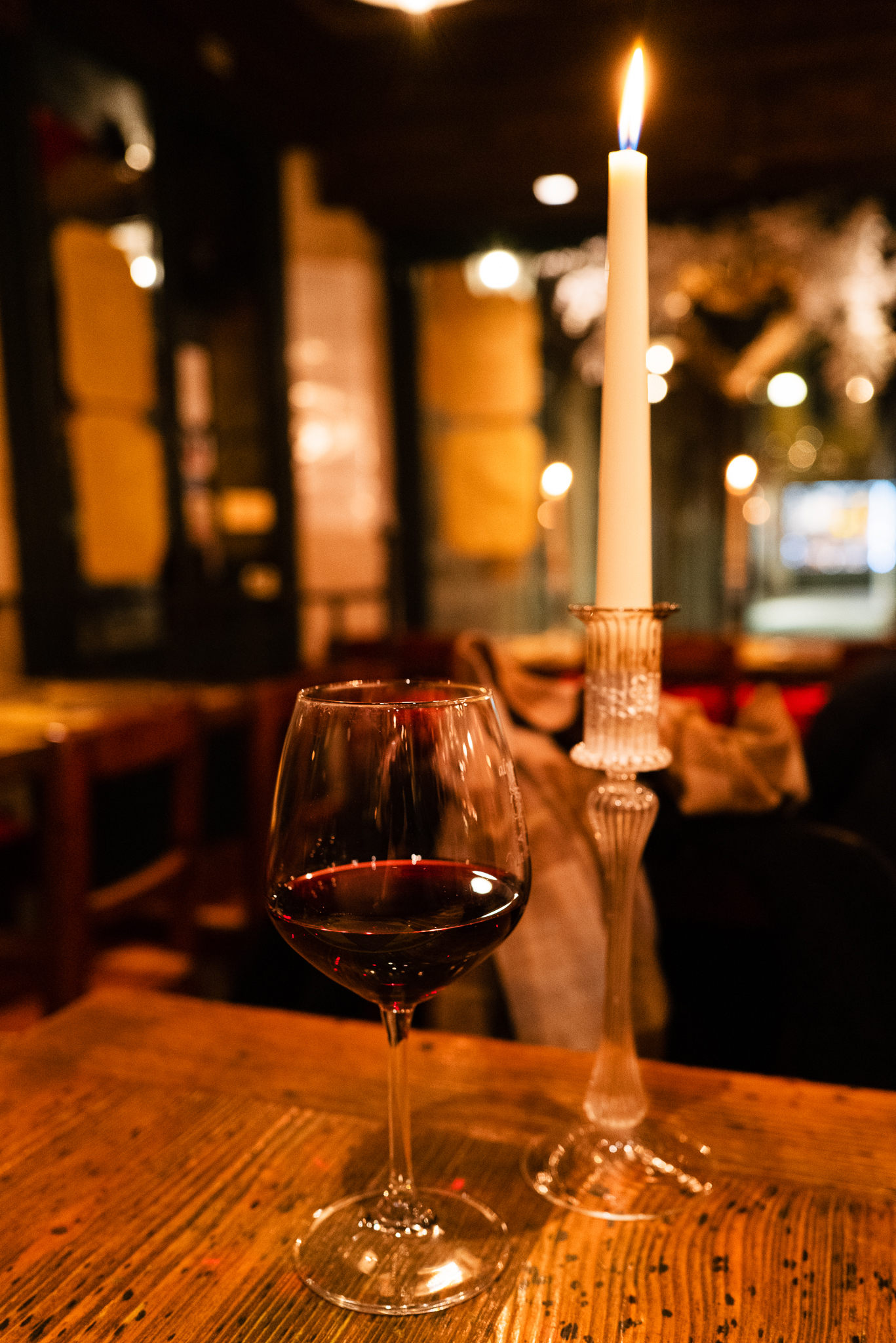 A glass of red wine next to a candle in a cosy restaurant.