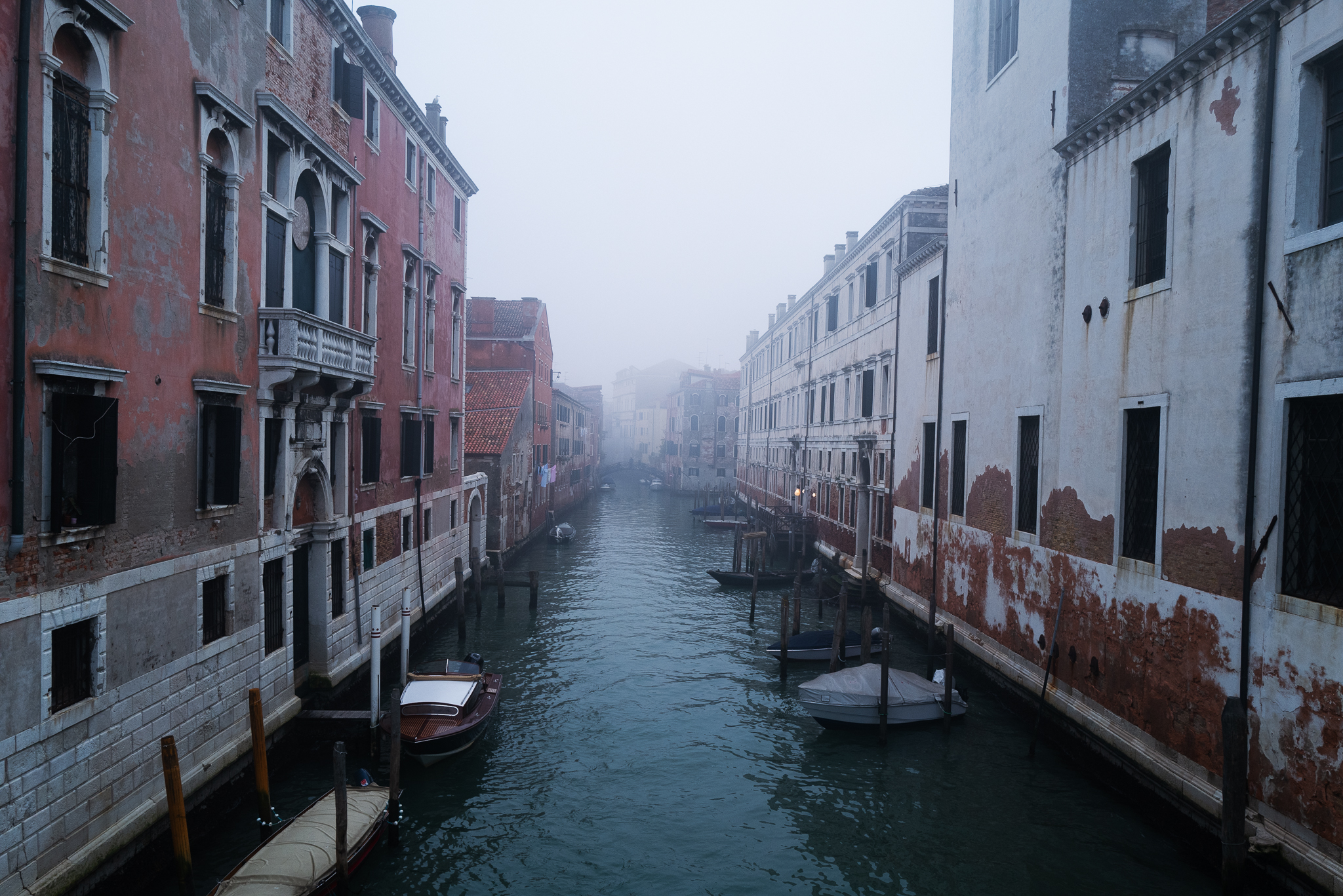 A foggy canal of Venice with a red house.