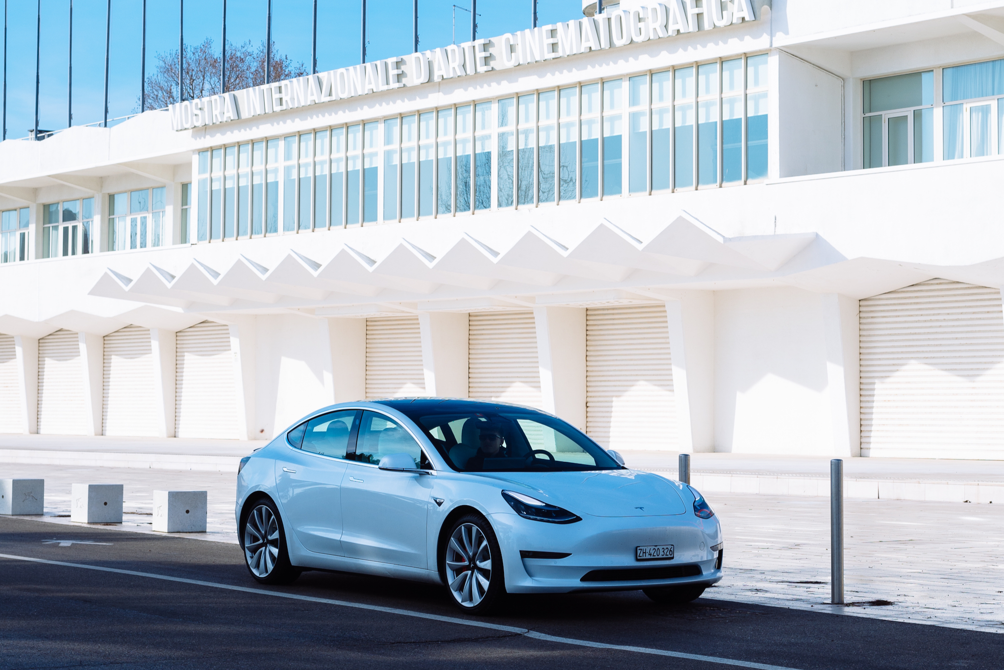 White Tesla Mode 3 in front of the white Palazzo del Cinema on Venice Lido.